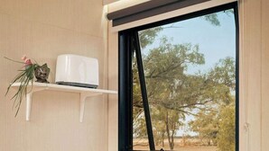 A compact kitchen with a sink, a Hisense dishwasher, a window with a view of trees, and a shelf with a toaster and a decorative frog.