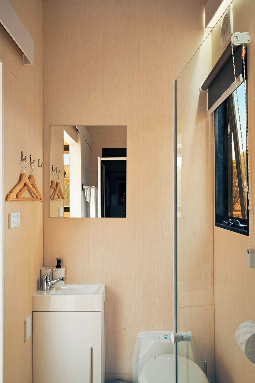 Une salle de bain moderne avec une douche en verre, un lavabo avec un miroir et des porte-manteaux en bois fixés au mur.