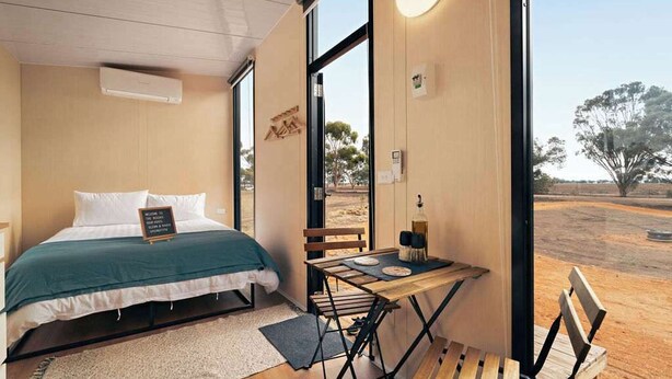 A bedroom with a bed, a table with chairs, and a view of the outdoors.