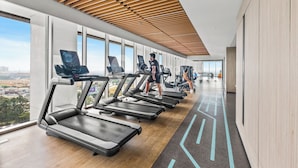 A modern gym with treadmills aligned along a wall with large windows offering a city view. - The Smith Luxury SkyView Apartments (Tangerang)