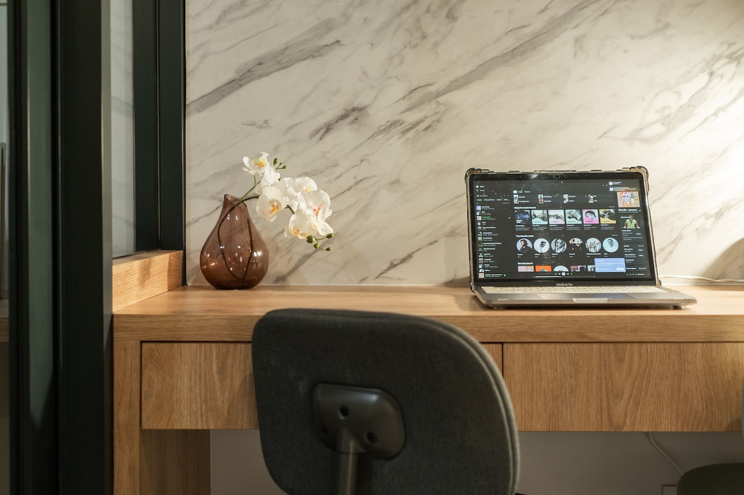 A laptop on a wooden desk with a marble wall in the background.