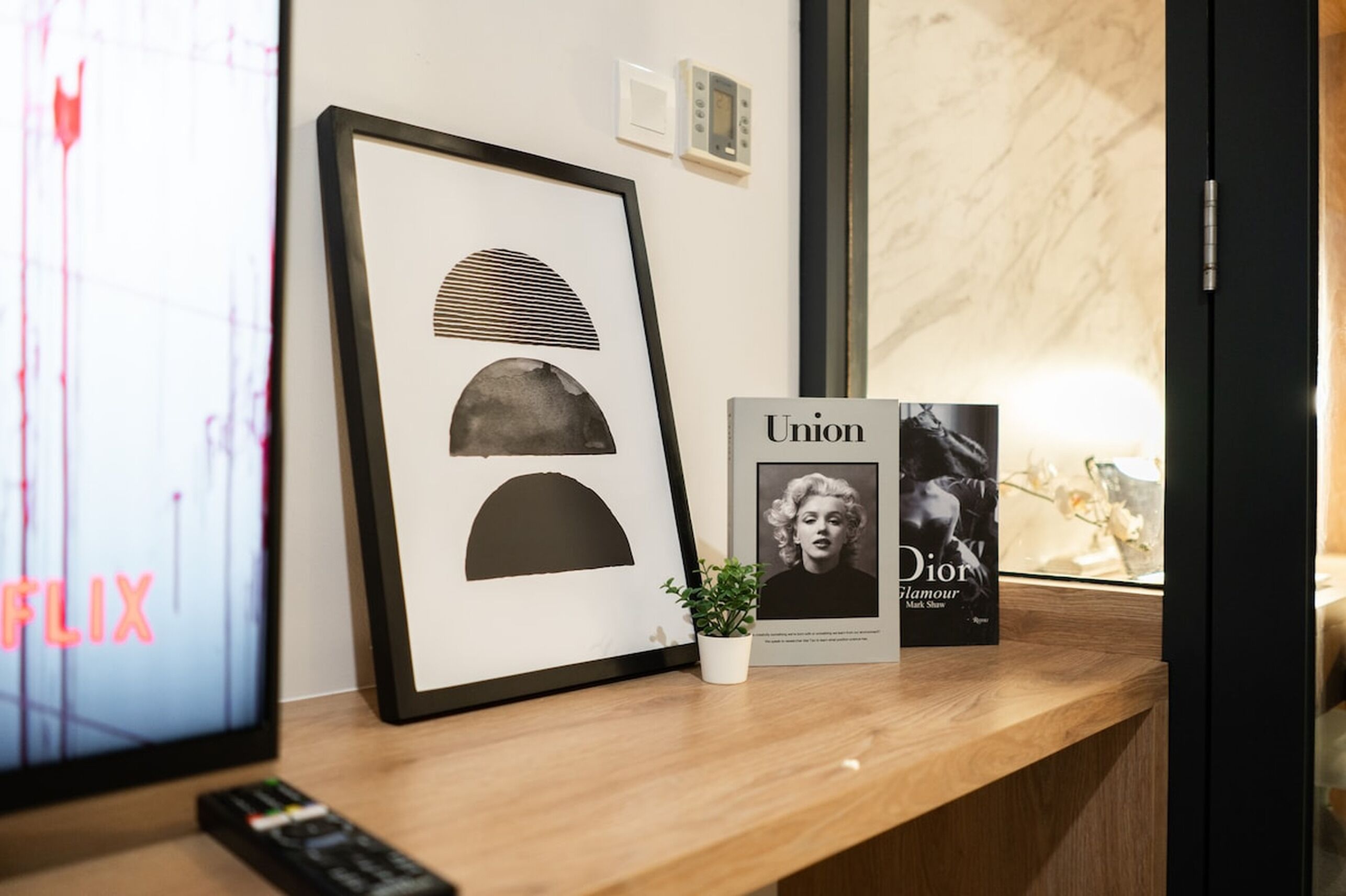 Ein gerahmtes Kunstwerk, ein Buch mit dem Titel 'Union Dior Glamour' und ein kleiner Topfpflanze auf einer Holzoberfläche.