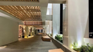 A modern indoor space with a wooden slatted ceiling, a long corridor with benches, and a view of a cityscape through large windows. - The Smith Luxury SkyView Apartments (Tangerang)