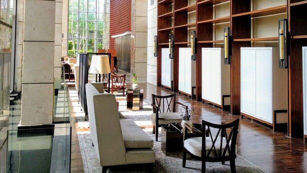 Un'ampia hall dall'arredamento moderno, con una lunga zona relax dotata di divani e poltrone, un tappeto decorato e una grande libreria in legno.
