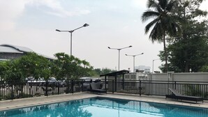 Una piscina con recinzione nera, circondata da alberi e un edificio sullo sfondo.