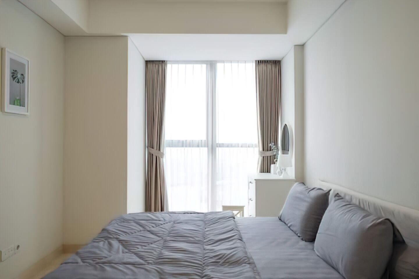 Quarto com cama, mesa de cabeceira, espelho e janela com cortinas.