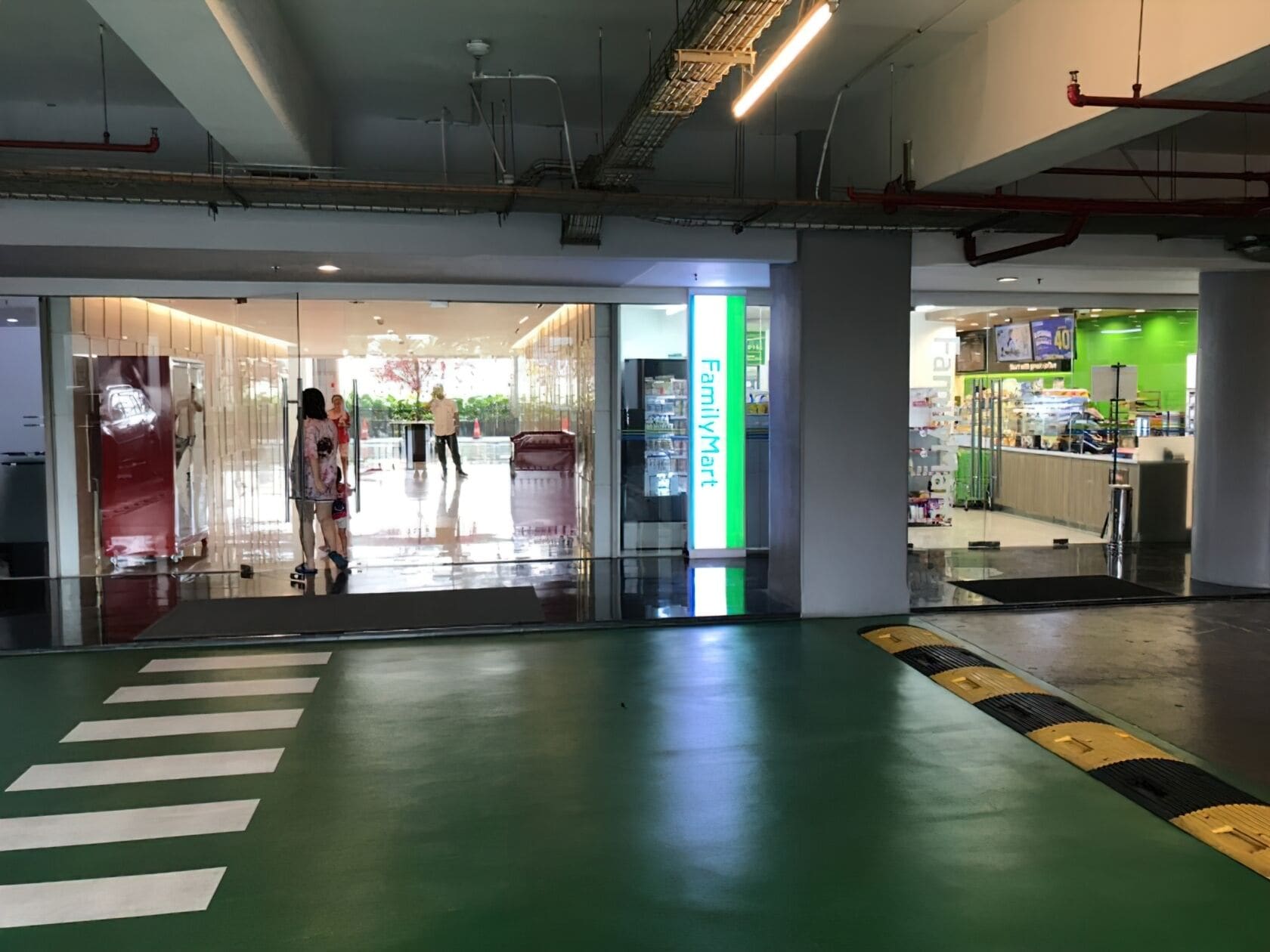 Un espacio interior amplio con suelo verde, una tienda FamilyMart y una salida visible.