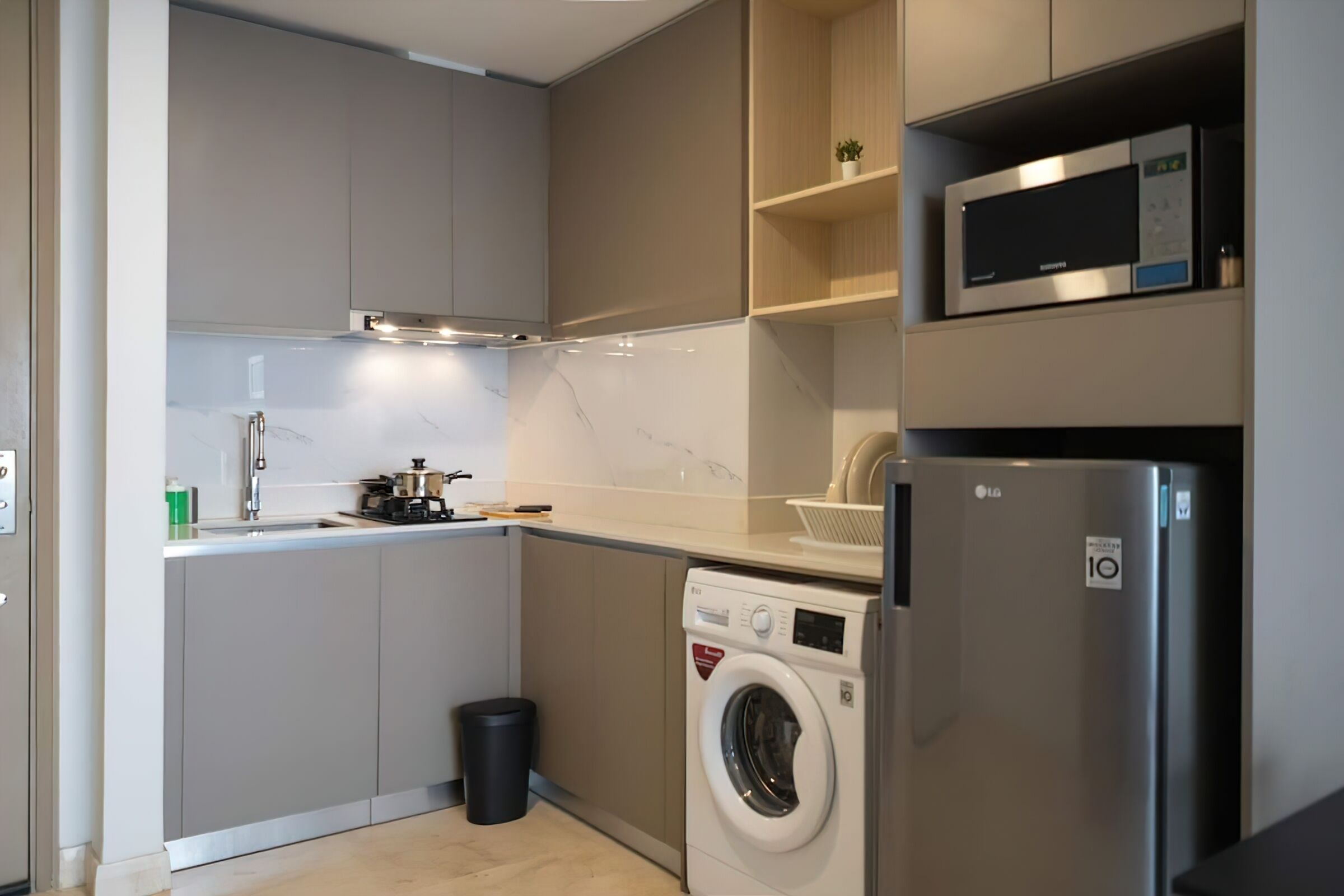 Een kleine keuken met een wasmachine, een magnetron en een koelkast.