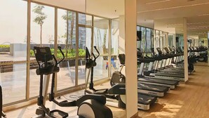 A gym with stationary bikes and treadmills arranged in rows, large windows offering views of the outside. - Seaview GoldCoast Residence in Jakarta (Jakarta)