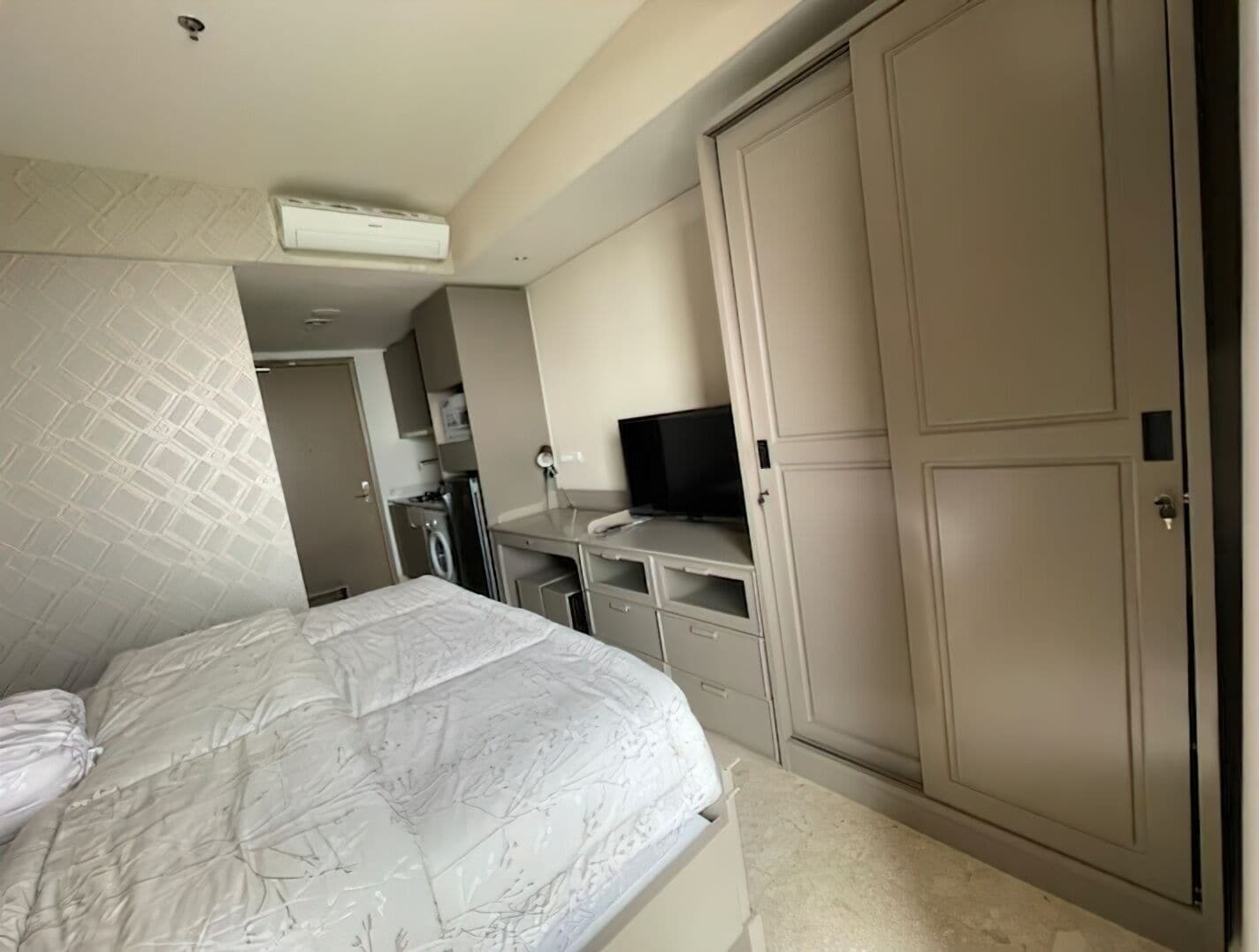 A bedroom with a bed, a television, a wardrobe, and a washing machine.