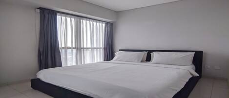 A bedroom with a bed, a window with curtains, and a ceiling light.