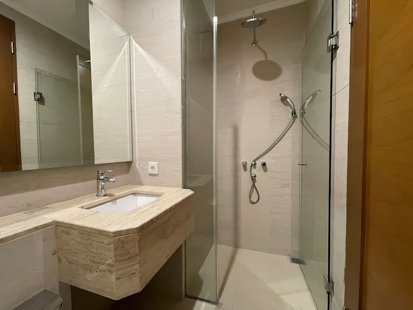 A modern bathroom with a marble sink, a glass shower enclosure, and a large mirror.