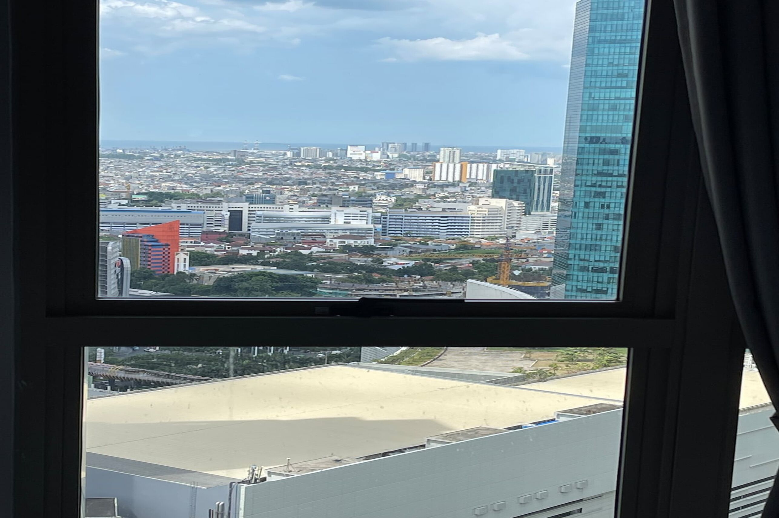 Une vue sur la ville à travers une fenêtre, avec des gratte-ciel, un ciel dégagé et une vue lointaine sur la mer.