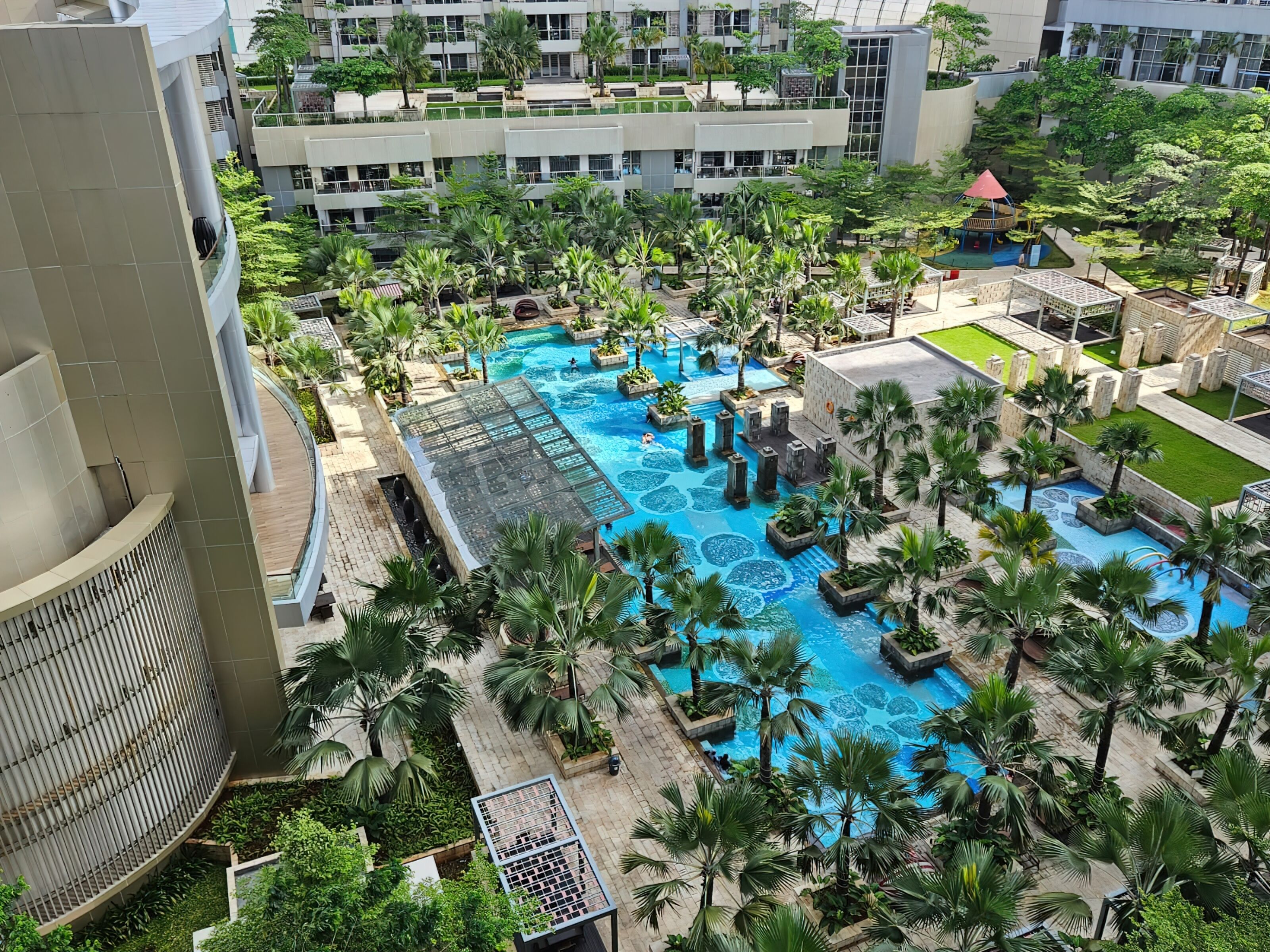 A rooftop pool area with palm trees and a glass-roofed structure.