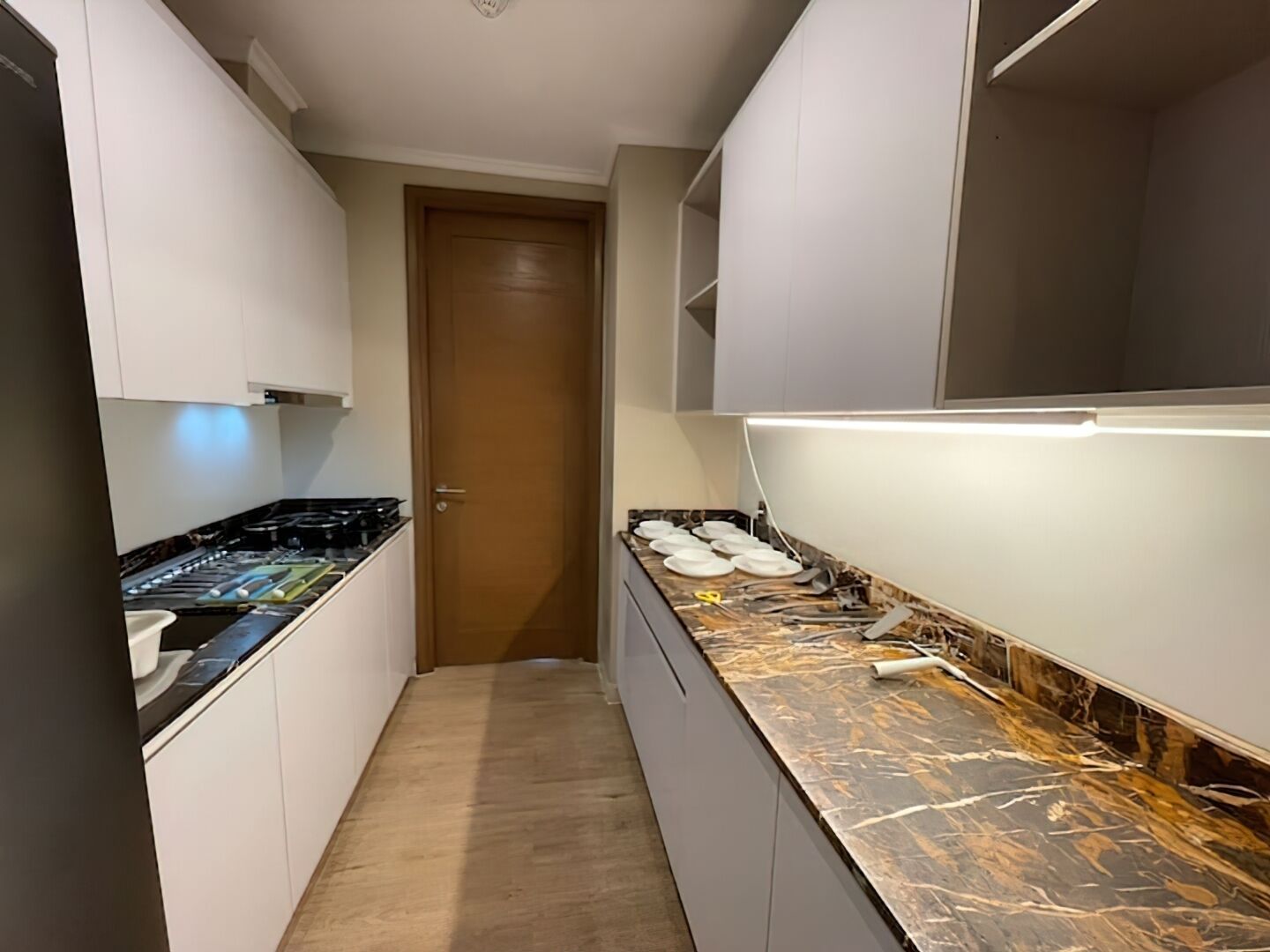 A narrow kitchen with white cabinets, a black countertop, and a wooden door at the end.