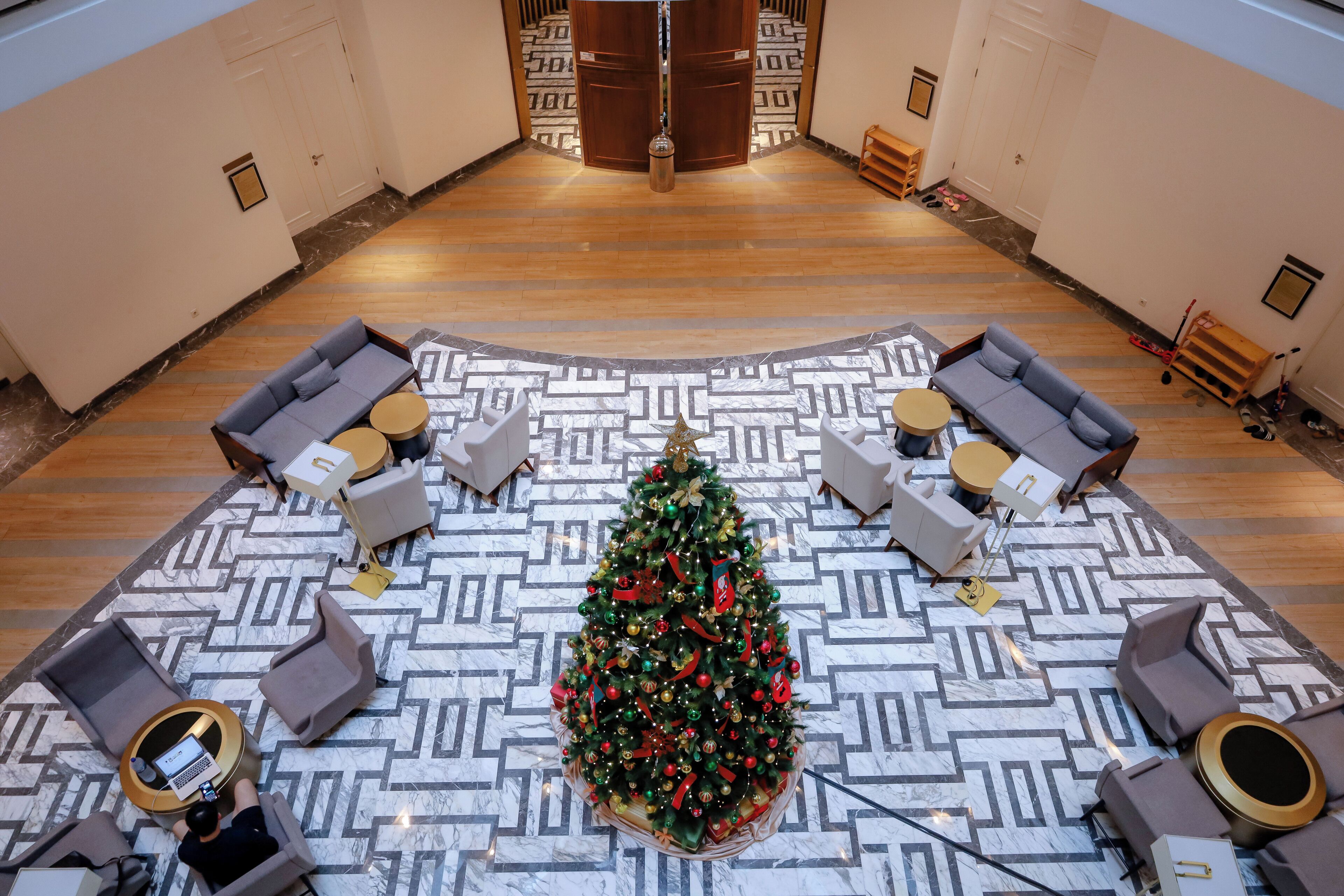 A spacious lobby with a central Christmas tree, seating areas, and a patterned floor.