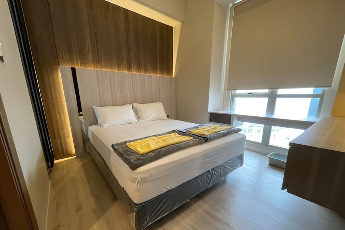 A modern bedroom with a large bed, wooden headboard, and a view of the outdoors through a window.