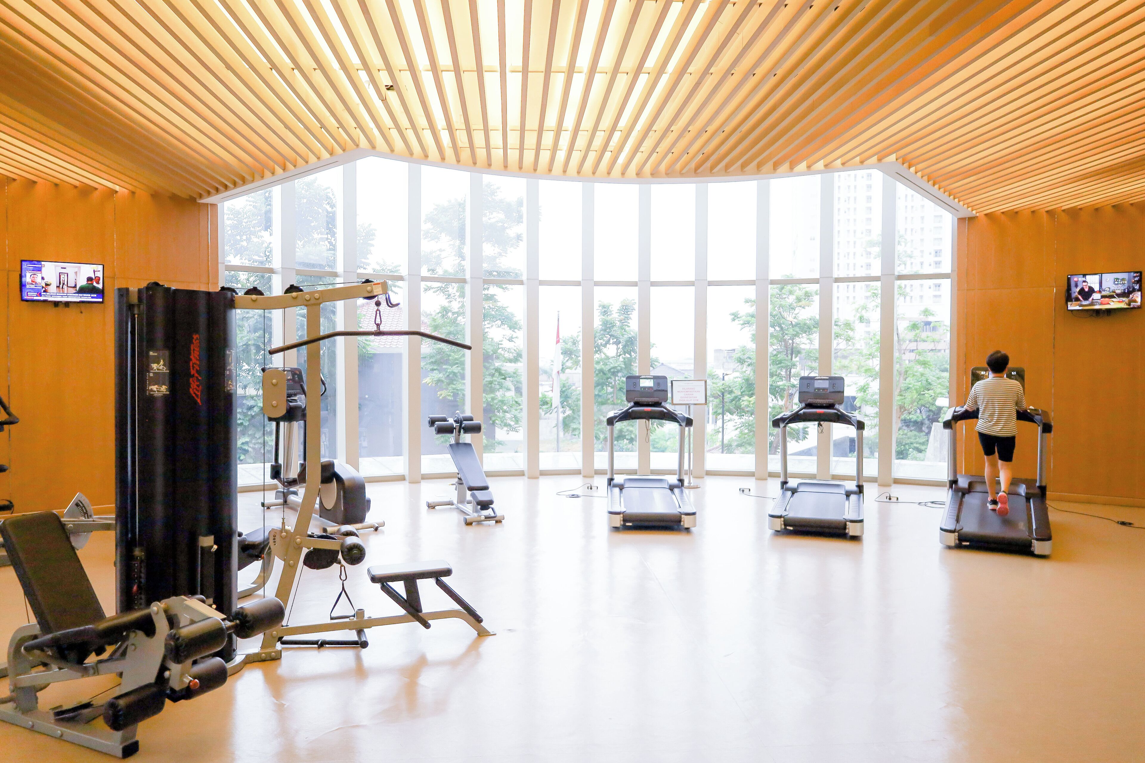 Un gimnasio con cintas de correr, máquinas de pesas y ventanas amplias.