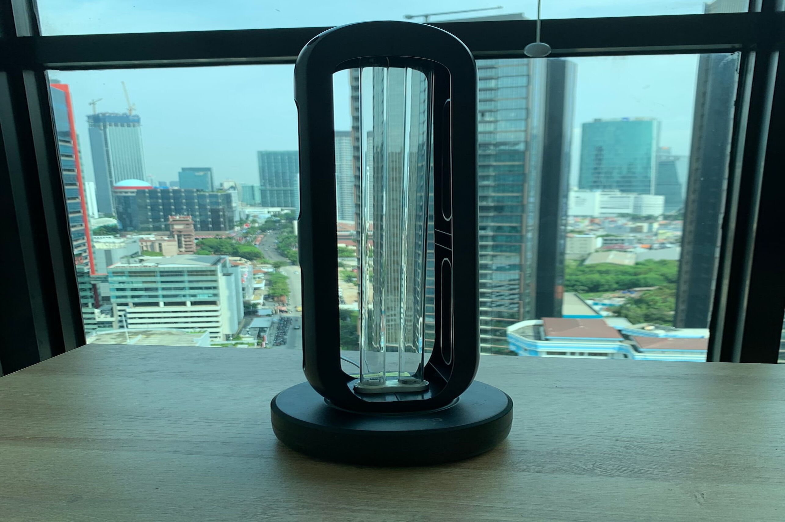 A modern, minimalist air purifier on a wooden table with a cityscape view through large windows.