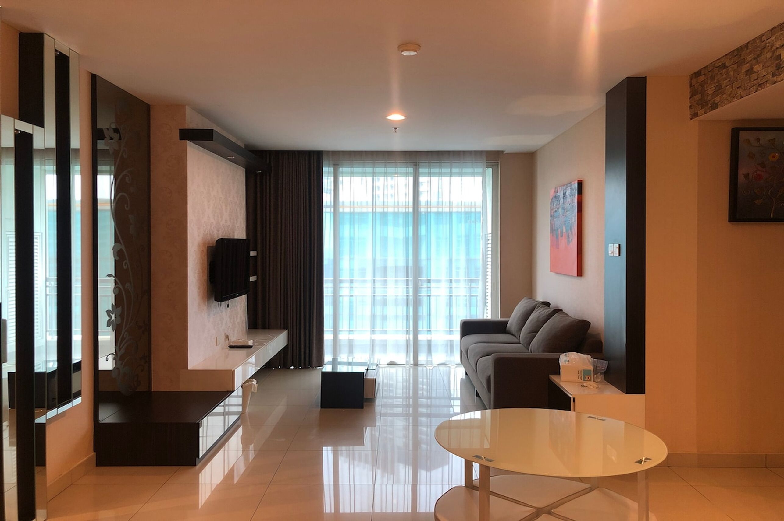 Una sala de estar moderna con un sofá, una mesa de centro de vidrio y un televisor montado en la pared.
