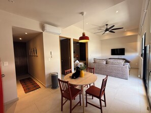 A modern living space with a dining area, a sofa, a television, and a ceiling fan.