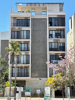 Un hôtel à plusieurs étages doté de balcons, d’un élément vertical central et d’une signalétique indiquant le nom et l’emplacement de l’hôtel.