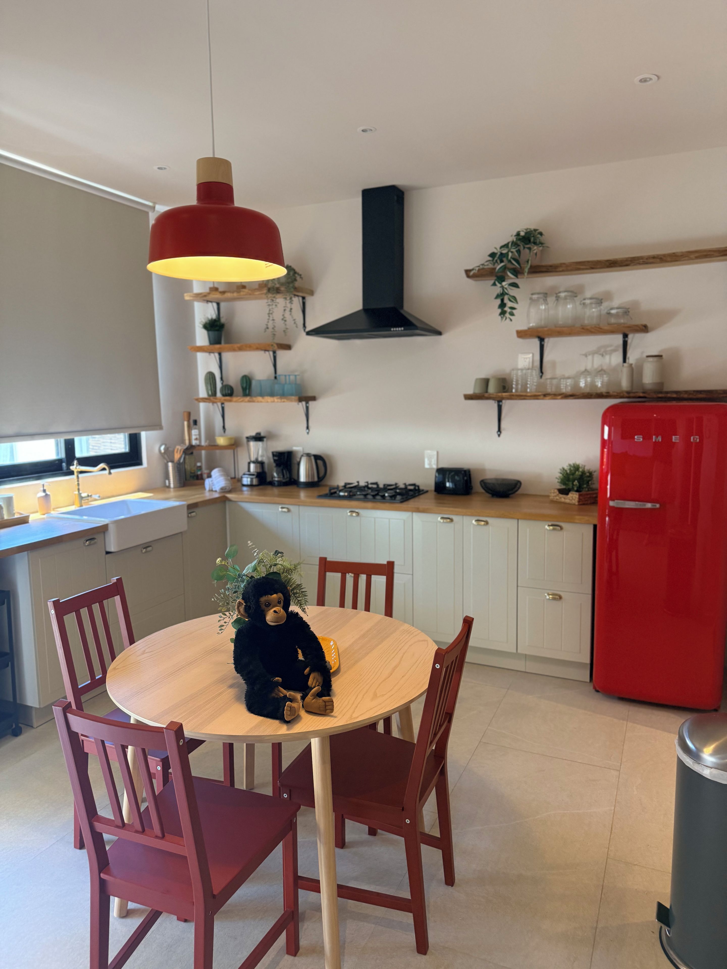 A modern kitchen with a round wooden table, red chairs, a red refrigerator, and various kitchen appliances.