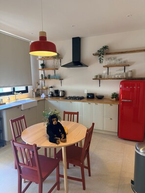 A modern kitchen with a round wooden table, red chairs, a red refrigerator, and various kitchen appliances.