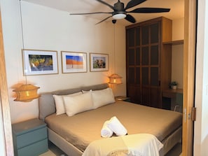 Une chambre à coucher comprenant un lit, des tables de chevet, un ventilateur de plafond, des tableaux encadrés et une armoire.