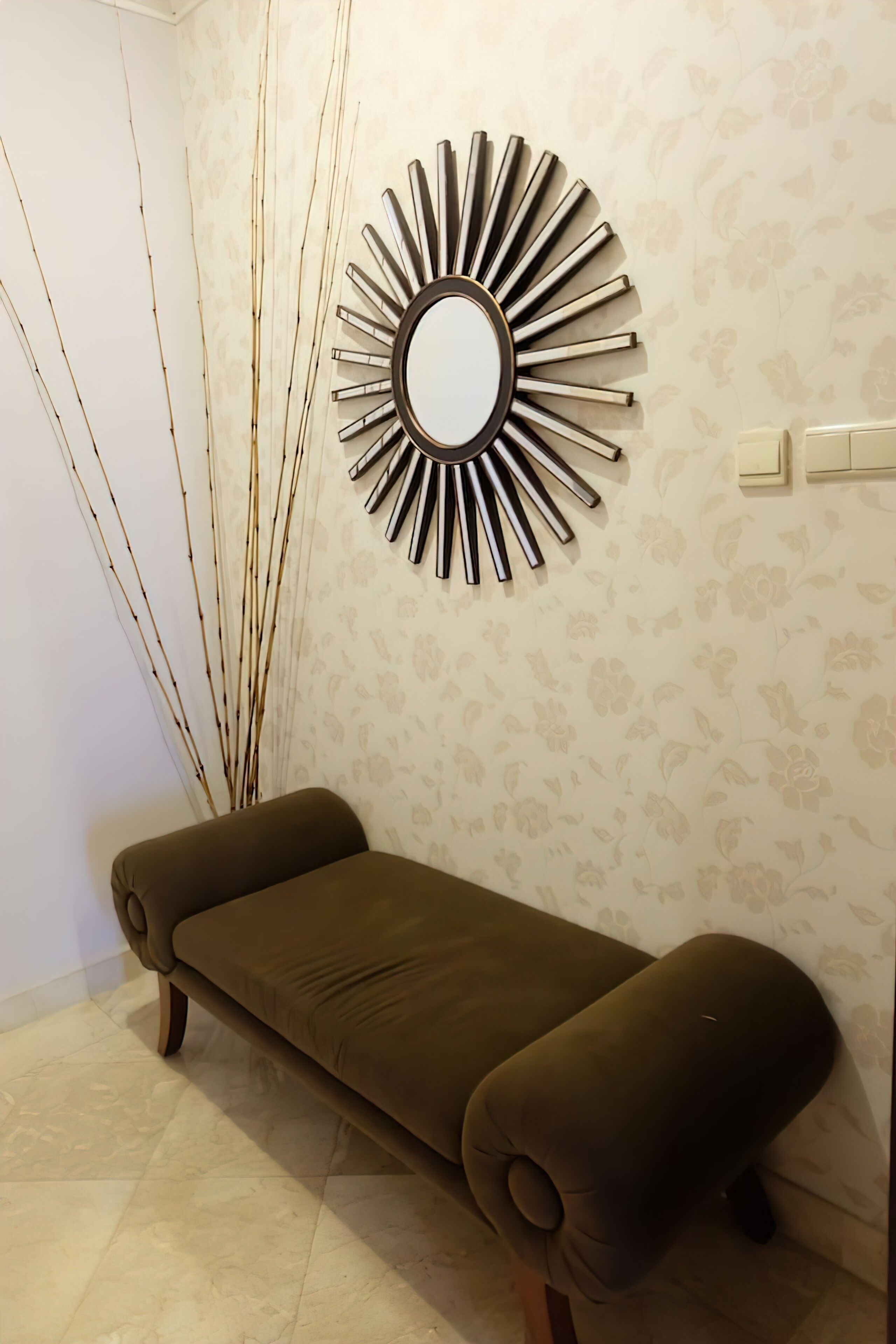 A room with a sofa, a wall-mounted mirror, and a wall with floral wallpaper.