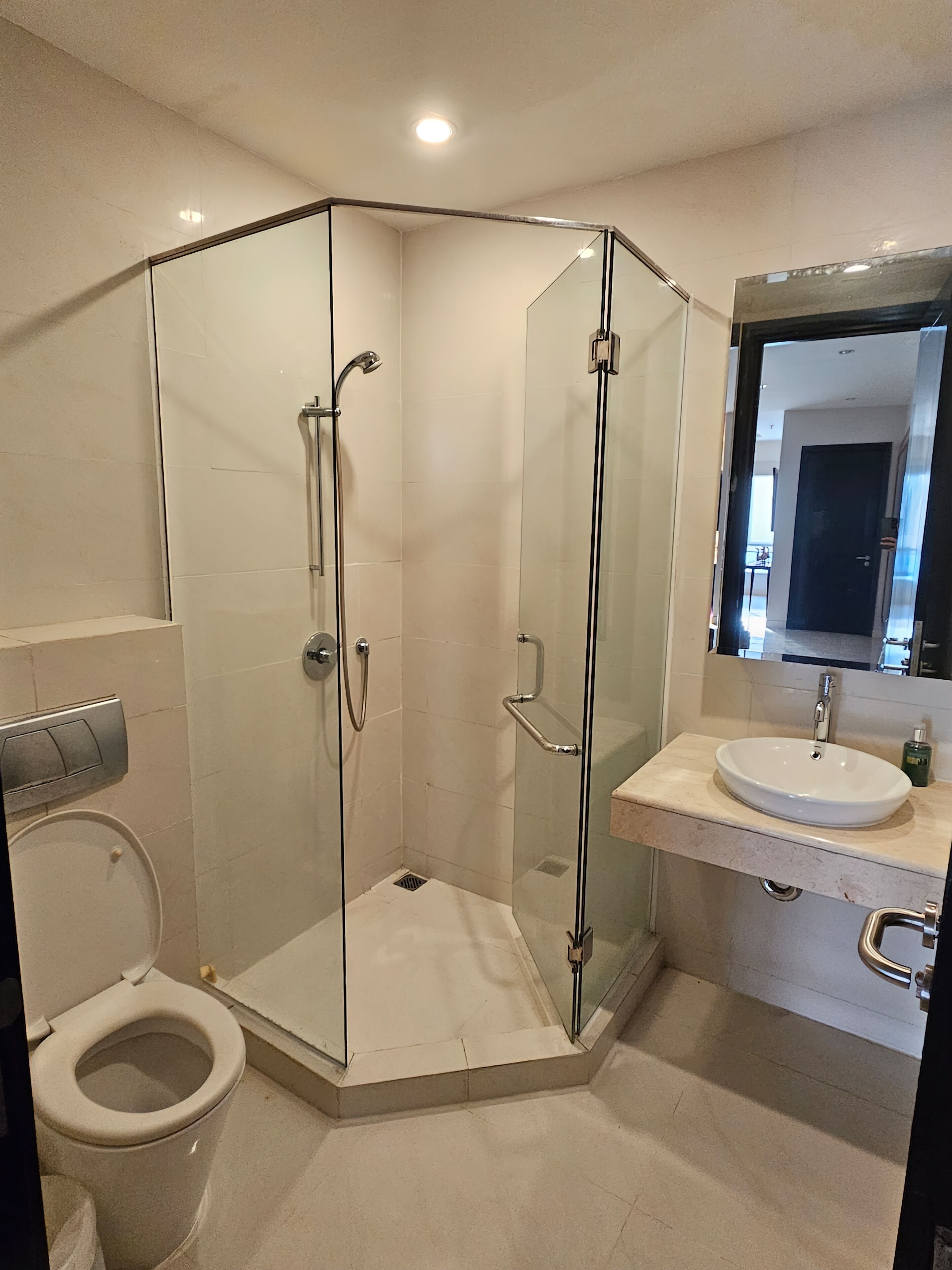Un baño moderno con ducha de vidrio, inodoro y lavamanos con espejo.