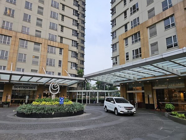 A modern hotel entrance with a covered driveway, a white car parked in front, and a sign for 'Somerset'.