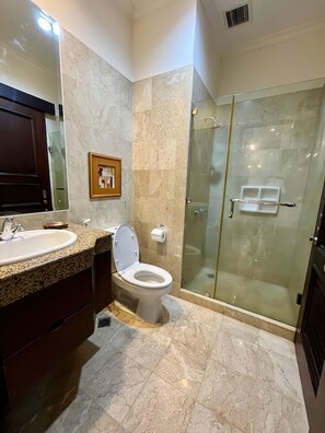 A bathroom with a marble floor, a sink, a toilet, and a glass-enclosed shower.