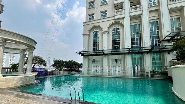 A swimming pool with a clear blue water, surrounded by a building with large windows and a covered area with columns. - Somerset Berlian Suites Jakarta (Jakarta)
