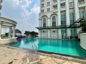A swimming pool with a clear blue water, surrounded by a building with large windows and a covered area with columns.