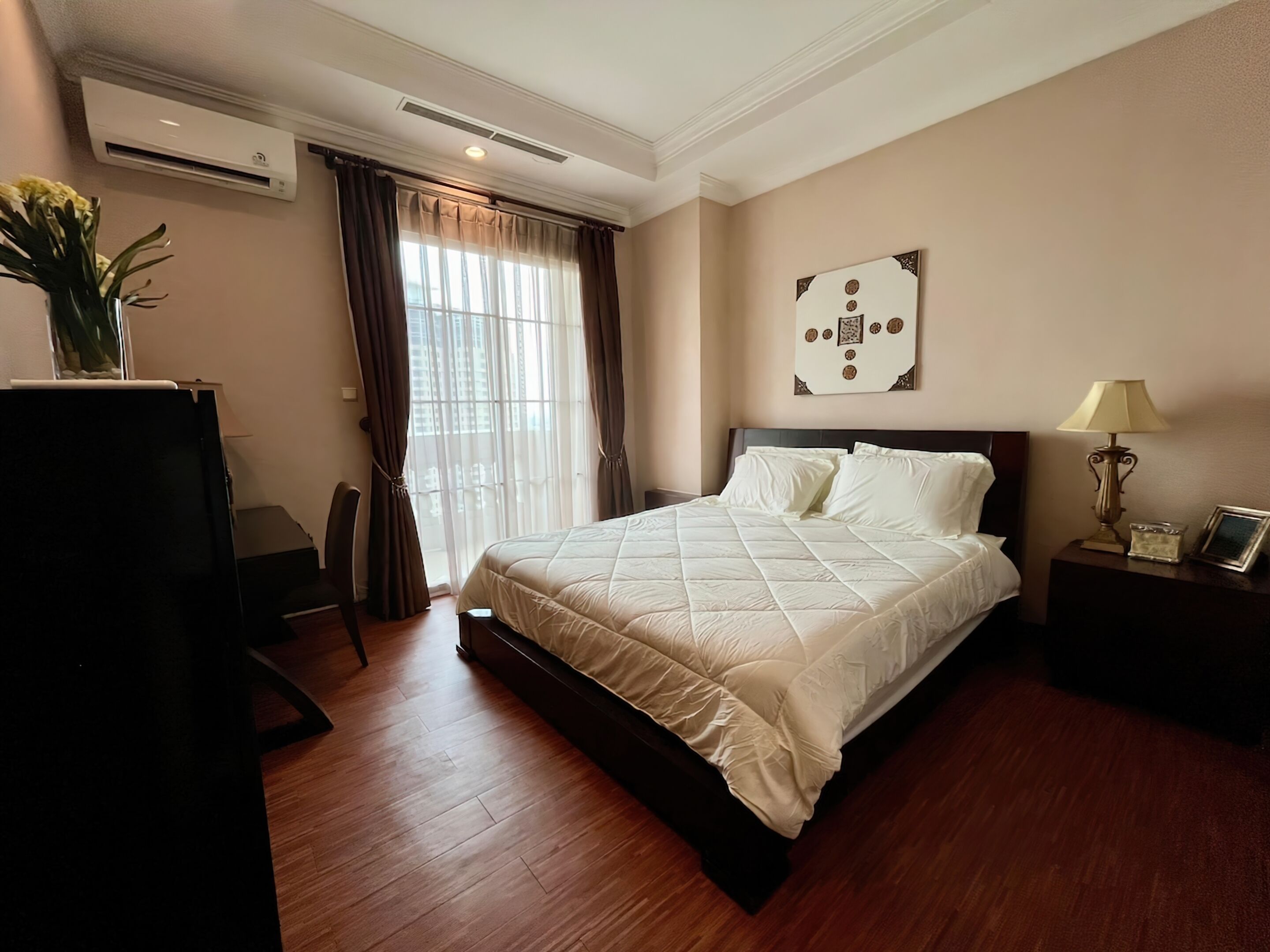 Habitación de hotel con una cama grande, una mesita de noche con lámpara, aire acondicionado en la pared y una ventana con cortinas.