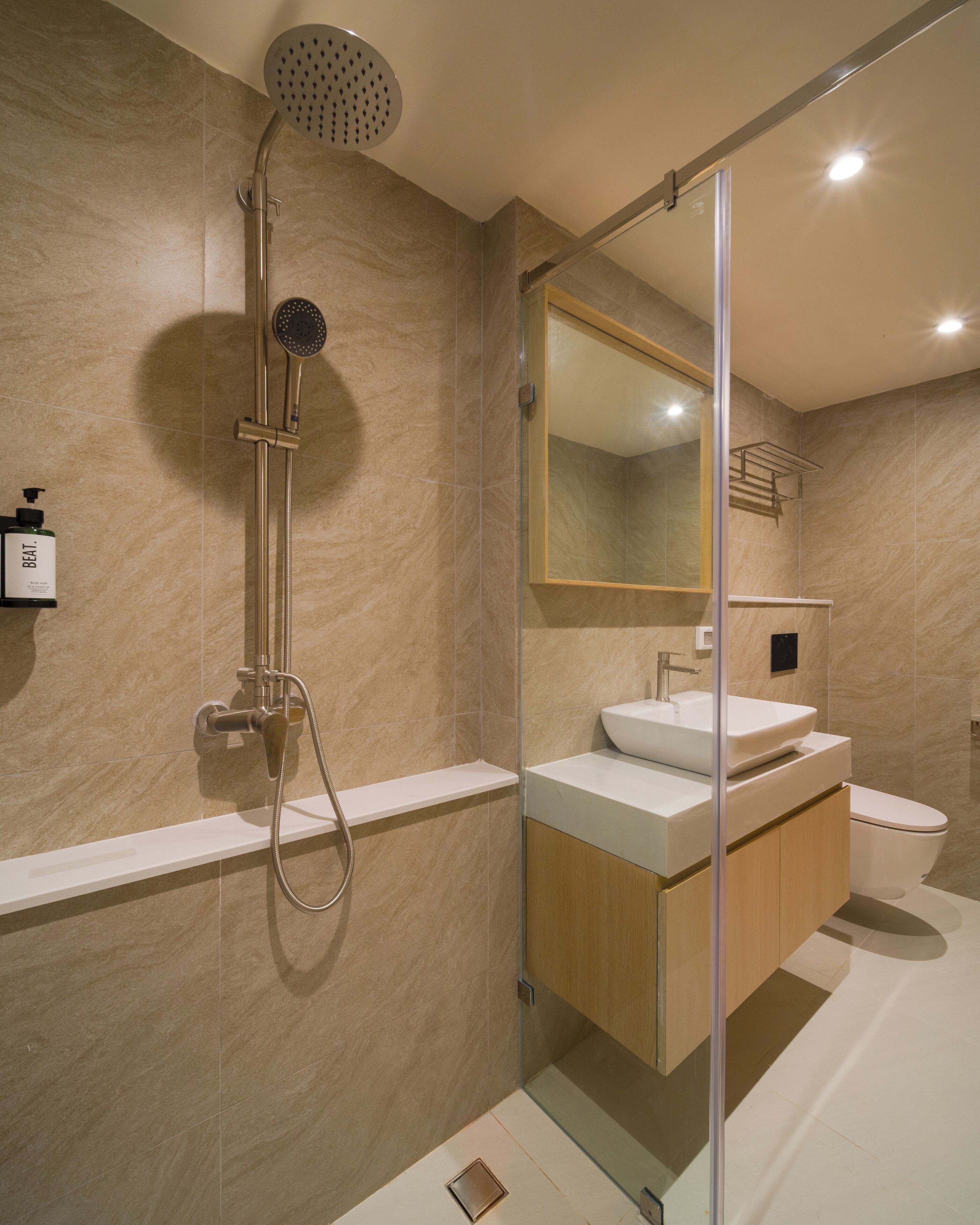 Un baño moderno con cabina de ducha de vidrio, un espejo grande y un mueble de tocador de madera.