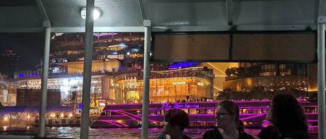 A nighttime view of a waterfront area with illuminated buildings and a covered seating area.