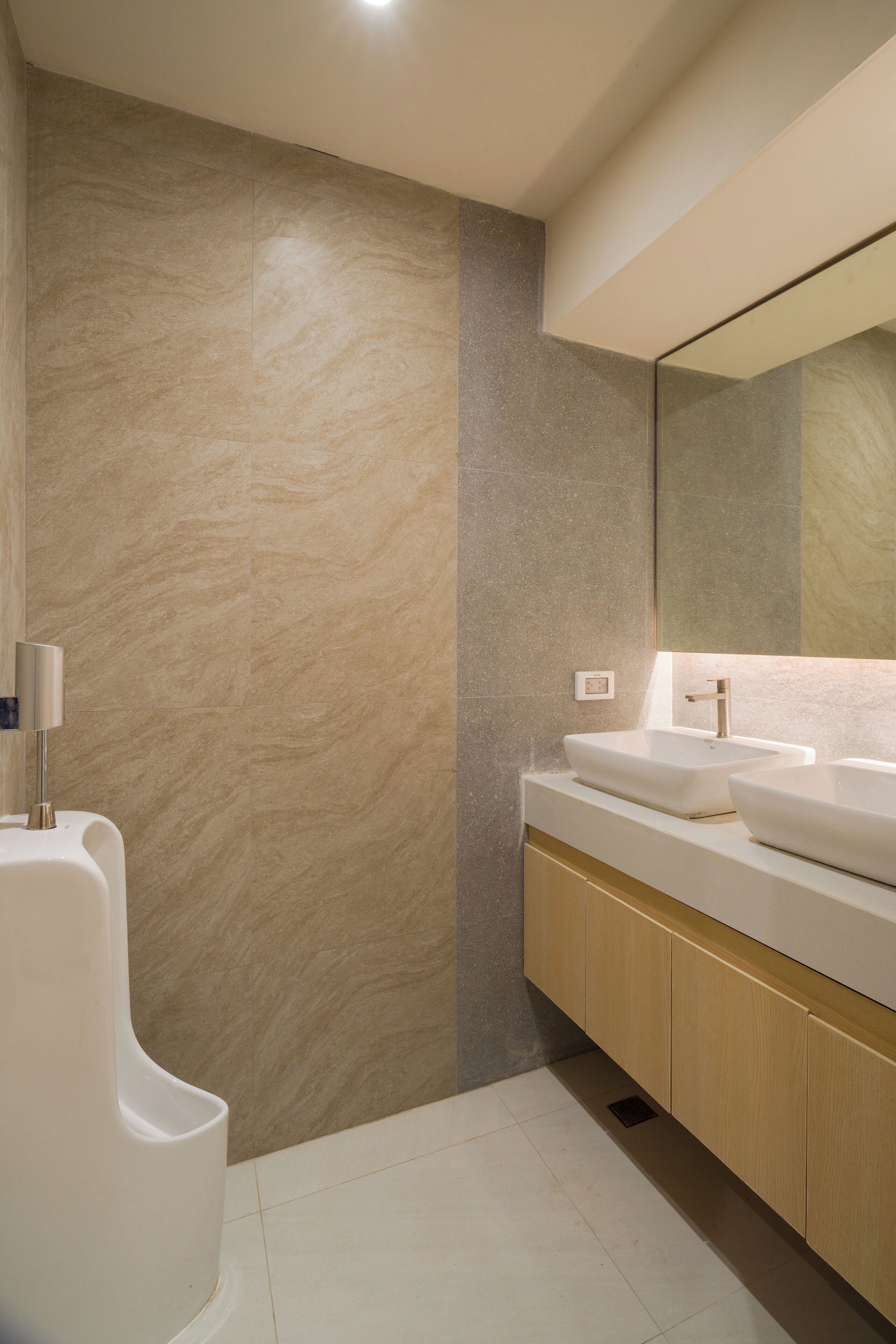 Un baño moderno con un espejo grande, dos lavamanos y un orinal.