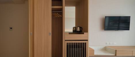 A modern hotel room with a wooden wardrobe, a flat-screen TV mounted on the wall, and a bedside table with a kettle.