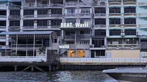 A multi-story building with balconies, a sign reading "BEAT Warii", and a water body in front.
