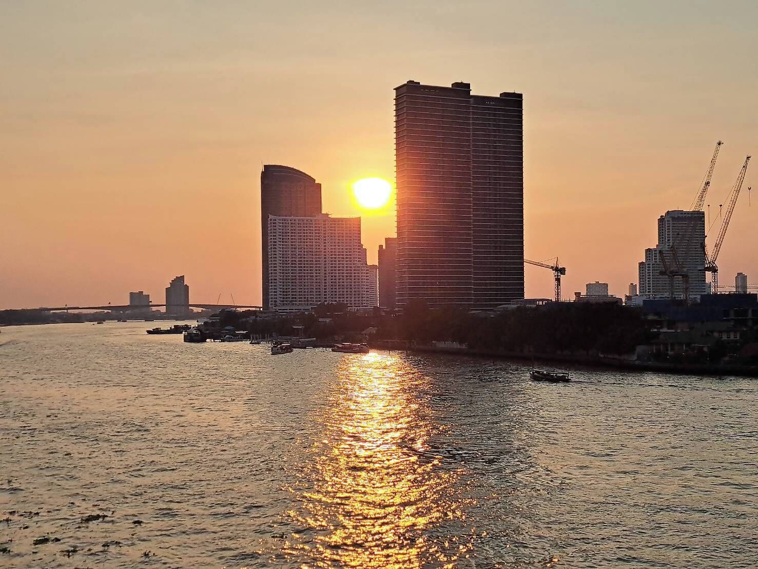 Ein Sonnenuntergang über einem Fluss mit modernen Gebäuden, darunter ein markanter Wolkenkratzer.