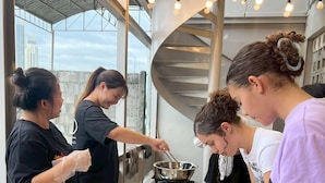 A group of people preparing food in a modern kitchen with large windows and industrial lighting.