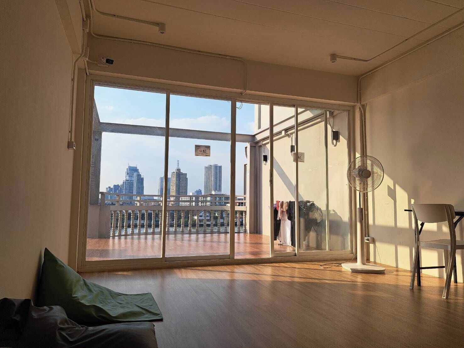 Una habitación con ventanas amplias, vistas al horizonte urbano, un ventilador y una silla.
