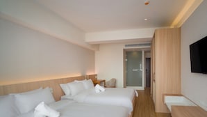 A hotel room with two beds, a TV mounted on the wall, and a wooden bench.