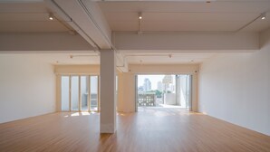 A spacious room with wooden flooring, large windows, and a view of the cityscape.