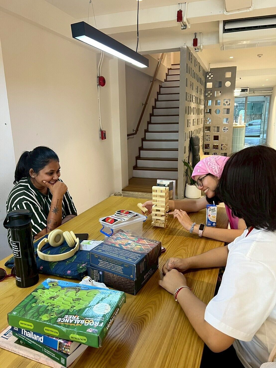 A group of people playing a board game at a wooden table in a room with a staircase and a modern design.