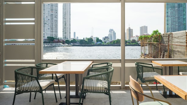 A terrace with a view of a river and city skyline, featuring tables and chairs.