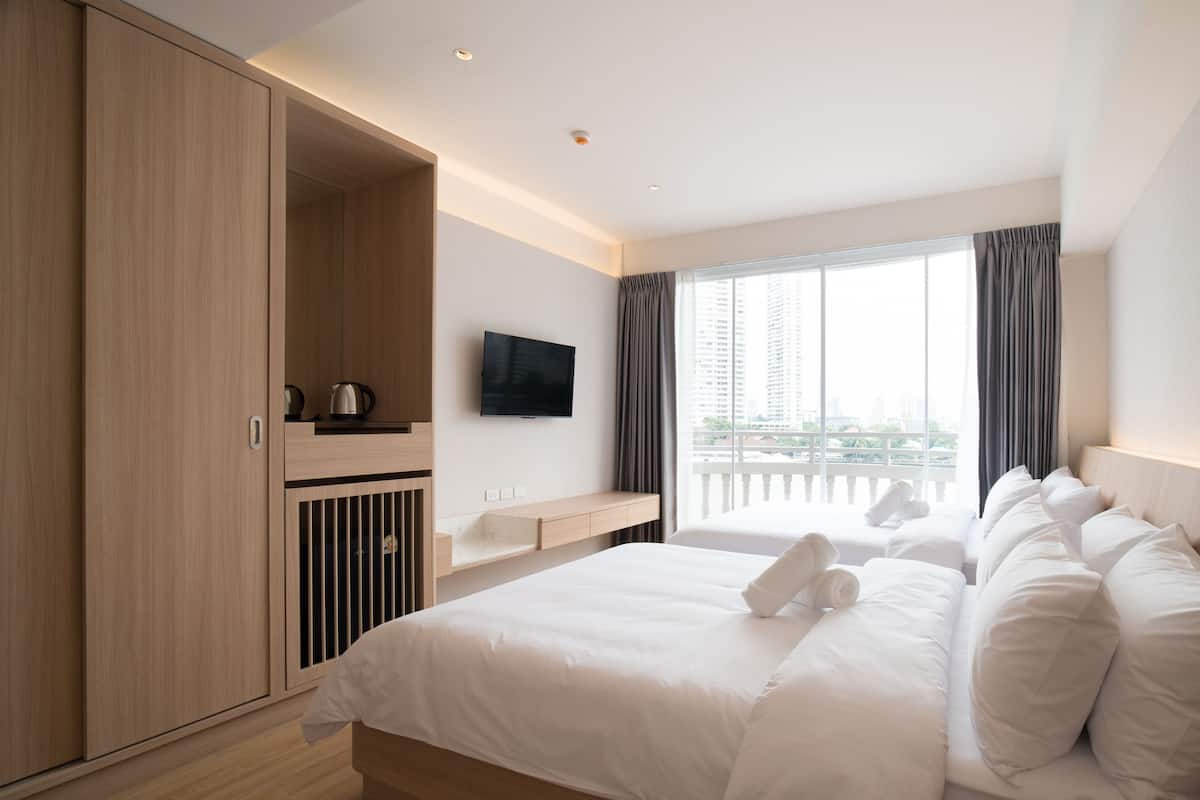 Ein Hotelzimmer mit einem großen Bett, einem an der Wand montierten Fernseher, einem Fenster mit Vorhängen und Blick auf die Stadt.