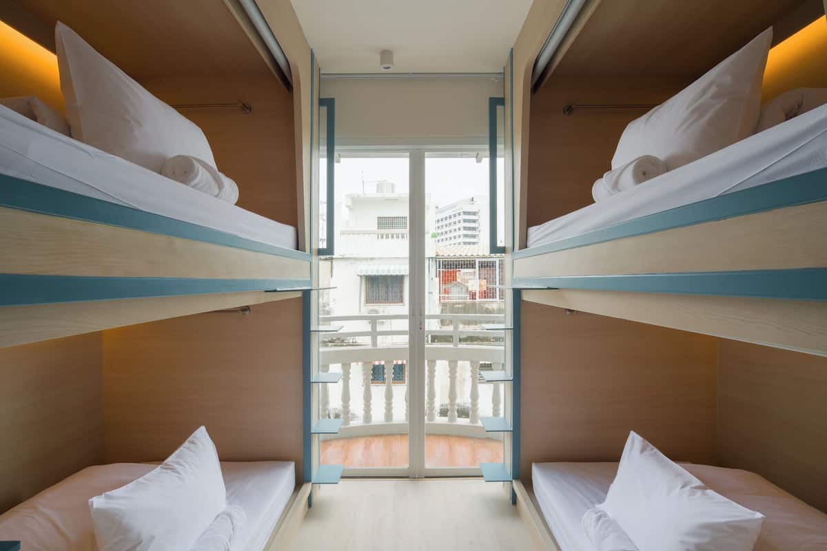 Ein Zimmer mit Etagenbetten, einem Balkon mit Geländer und Blick auf Gebäude.